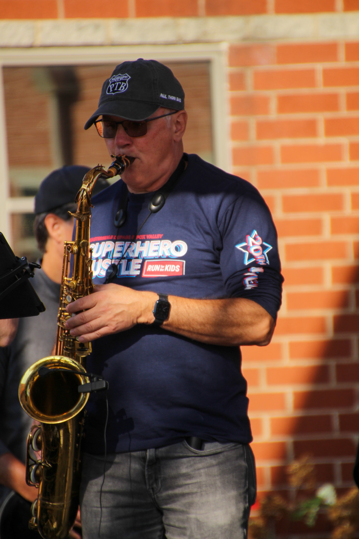 Man playing a saxaphone wearing a "superhero hustle 5k" shirt
